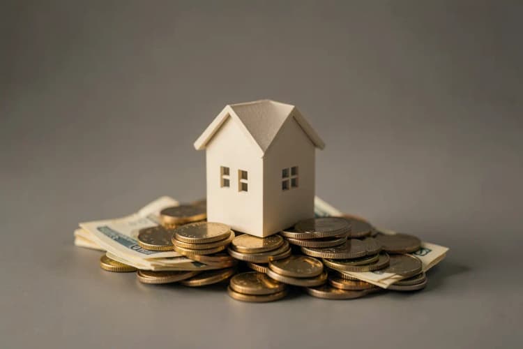 Uma casa em miniatura sobre um monte de moedas e notas de dinheiro.